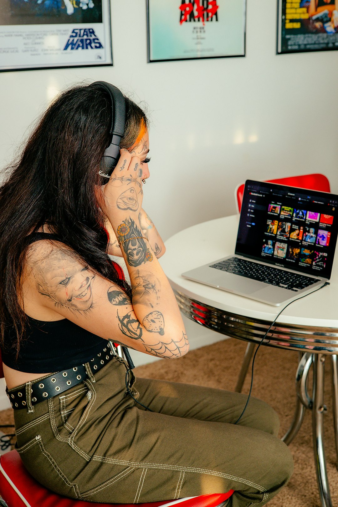 Woman with tattoos and headphones looking at music library on a laptop