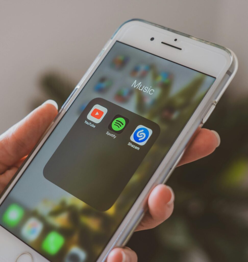Hand holding a smartphone displaying popular music apps like Spotify and Shazam in a close-up shot.