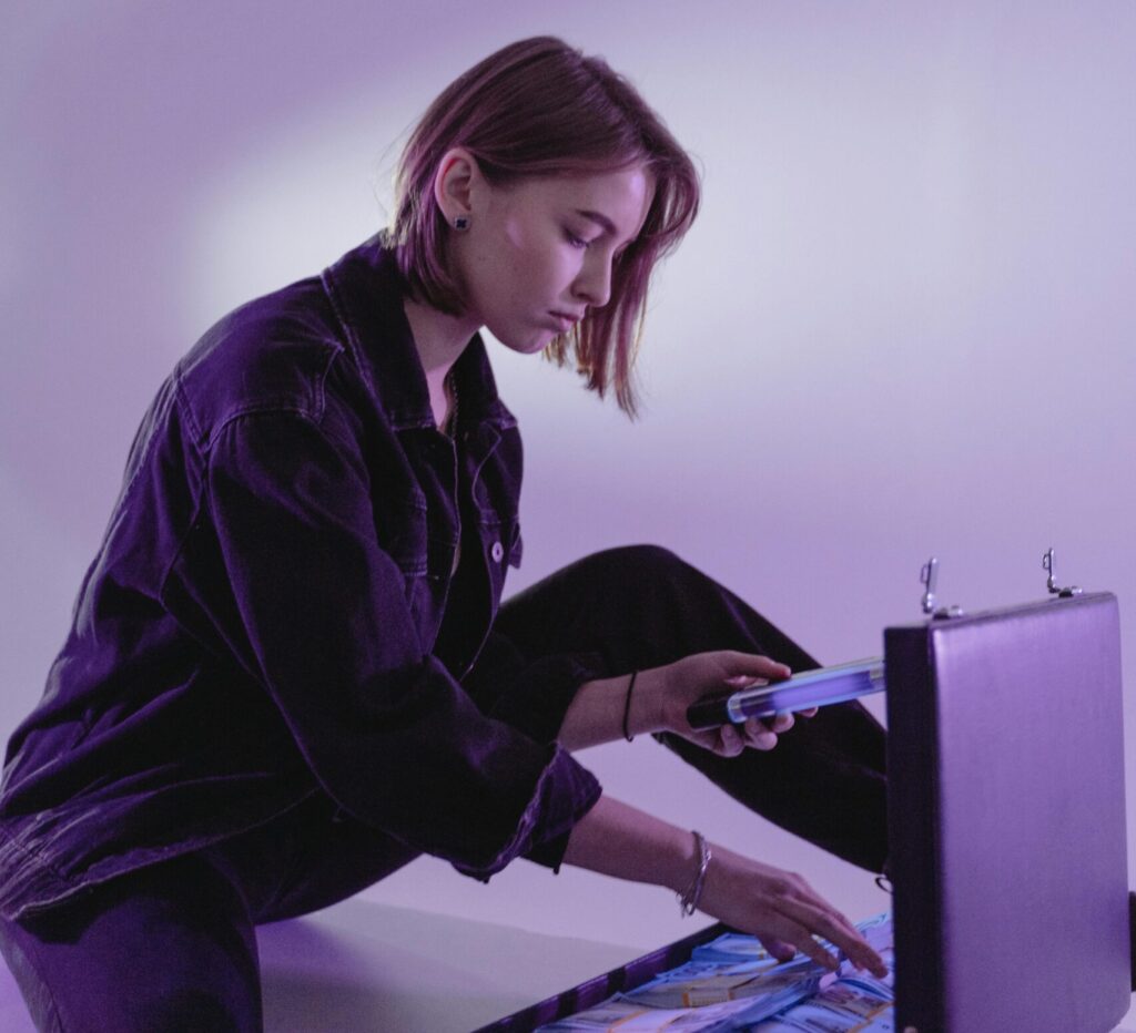 A young woman counts cash in a briefcase under purple lighting, suggesting business or finance themes.